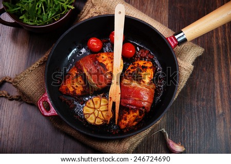 chicken breast wrapped in parma ham with cherry tomatoes, garlic and herbs in cast iron pan
