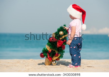 little girl draws a Christmas tree on the beach, a girl with a Christmas tree on a white sandy beach