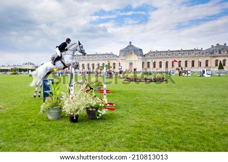 CHANTILLY, FRANCE - JULY 26, 2014: A rider competes in the Longines Global Champions Tour Grand Prix (Class 04) before the 18th century stalls of Chantilly.