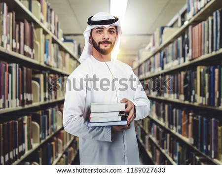 Arab student standing in library holding books on his arms. education concept.