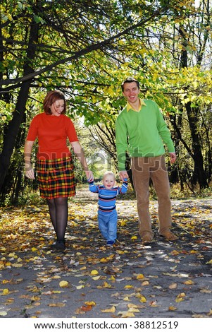 daddy and mom with  their little son  walking through the park in autumn