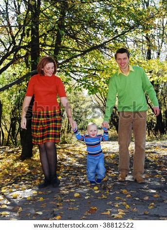 daddy and mom with  their little son  walking through the park in autumn