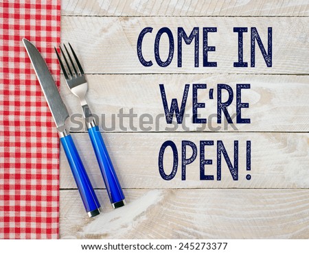 Come in - we are open ! Fork and knife on wooden background with text