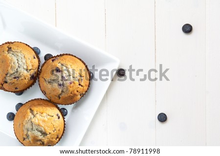 blueberry muffins, in a white square plate, on a white table, some berry on the table