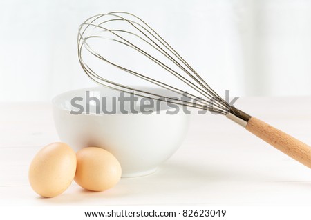 whisk, eggs, and bowl on a white table