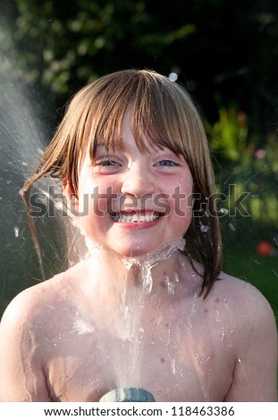 child playing with hosepipe in garden. boy play water games in summer on lawn