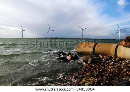 sewage waste pipe and offshore wind mills or turbines. coast with pollution and envirnmental friendly green energy production