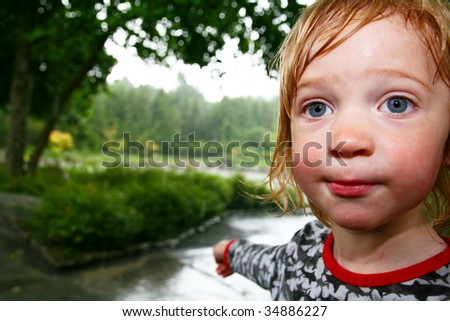 child in rain soaked with water. wet kid caught in storm in park or garden