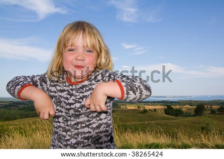 child with funny expression in landscape. boy laughing and making fun with sea and meadows and fields in background