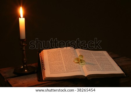 bible on table by candle light. old christian prayer book with flowers on page