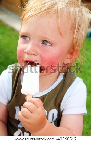 child eating ice cream. Messy small boy with blond hair biting lolly