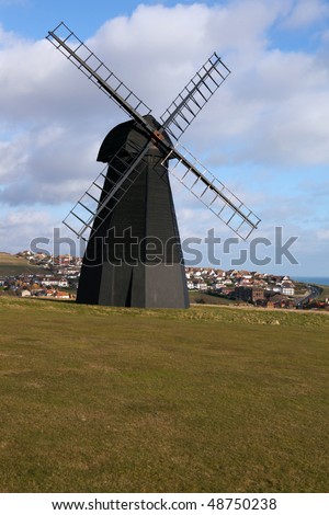 windmill in england with views of rottingdean town by brighton in sussex. old mill at top of hill with houses in background in england