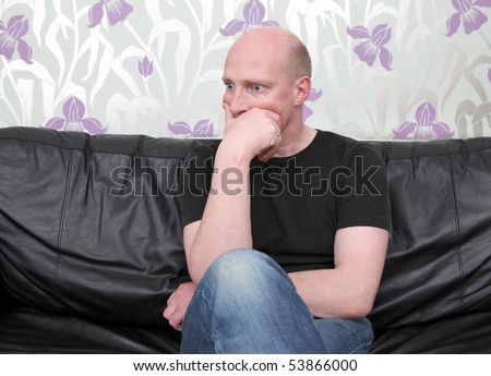 man sat on sofa watching something thinking or shocked. male on leather couch at home