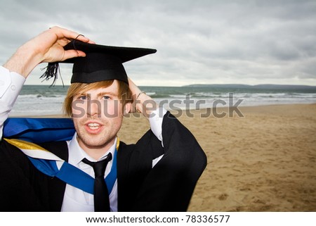 Student graduating with cap and gown on beach. University graduate celebrating