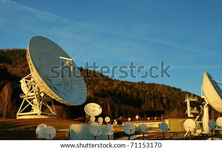 Satellite broadcasting dish at sunset time with mountains in background.