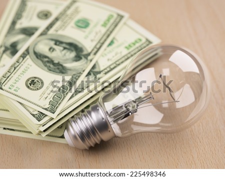 Incandescent light bulb in front of one hundred dollar bill stack