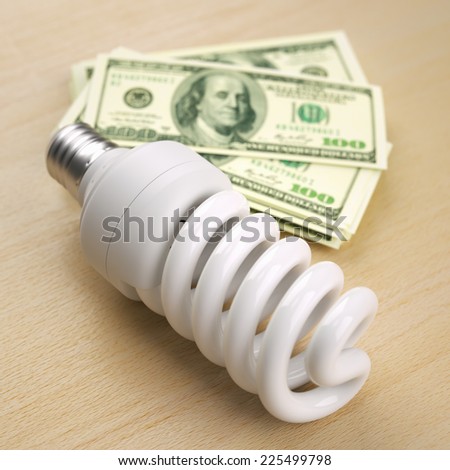 Compact fluorescent light bulb in front of one hundred dollar bill stack