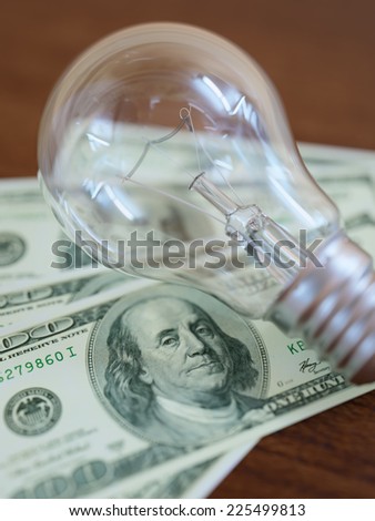 Incandescent light bulb on one hundred dollar bill heap