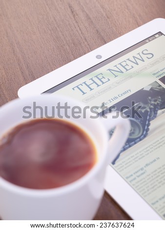 Tablet PC with launched news site or application on it and cup of coffee