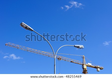 Urban view. Street lamp and lifting crane against slightly cloudy blue sky