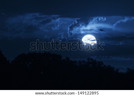 This big, bright moon illuminates the clouds and the night time sky as well as a commercial jet airliner on approach.