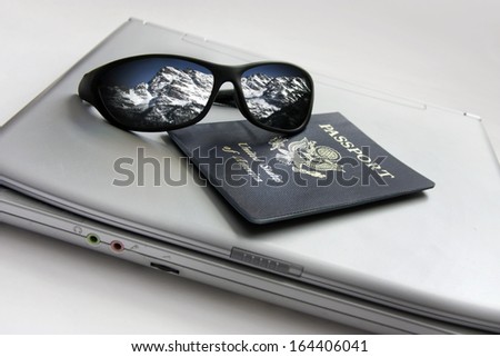 Sunglasses reflecting the snowy mountains and the possibility of a future ski vacation planned with passport and compact laptop on white background with selective focus. All components my own.
