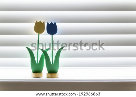 These two hand made wooden tulips appear to be embracing in the soft glow of a bright wooden window shade. Light reflections add an additional glow around each of them. Somewhat of a romantic theme.