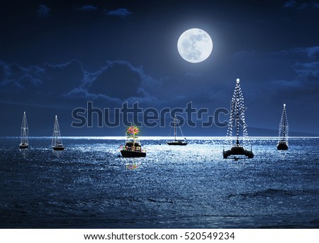 This photo illustration depicts a warm weather Christmas Holiday with deep blue sky and ocean at night, a full moon and a small group of boats decorated with lights. A Palm Tree as a Christmas Tree.