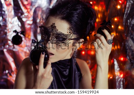 Mysterious young woman in black lace venetian carnival mask and silk elegant dress with Christmas decorations