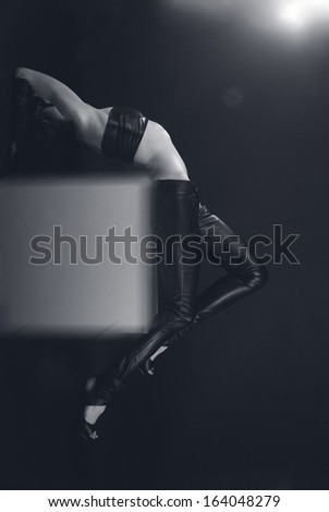 Beautiful young woman dressed black leather bustier and pants on  white cube. Athletic body