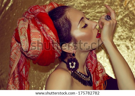 Portrait of passionate beautiful arabic young woman with gold makeup. Red clothes. Turban with ornament. Silver ring, earrings and necklace with precious jewels
