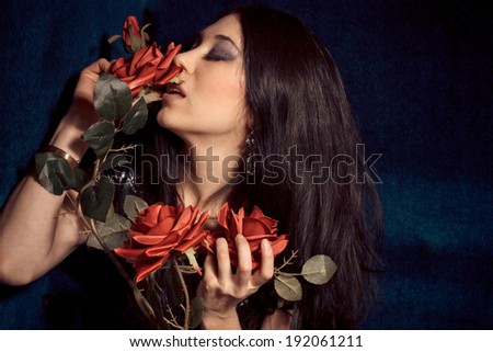 Young beautiful sexy woman in black leather dress smelling red roses on the background of blue velvet. Sensuality. Pleasure