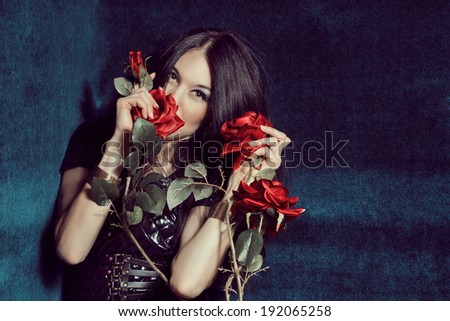 Young beautiful sexy woman in black leather dress with red roses on the background of blue velvet. Sensuality.