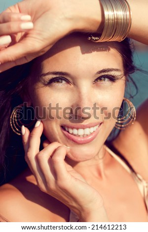 Outdoor closeup portrait of smiling beautiful young woman with gold bracelet and earrings.
