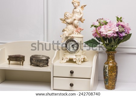 14 December, 2014.  Stage studio, Kiev, Ukraine. Modern antique interior of living room. White nightstand with carved  vintage boxes, clock with angels, vase with flowers.
