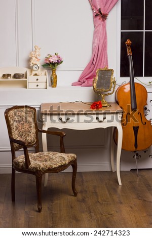 14 December, 2014. Stage studio. Kiev. Ukraine. Modern antique interior of living room. White nightstand with photo frame and red flower. Chair with upholstery. Violoncello.