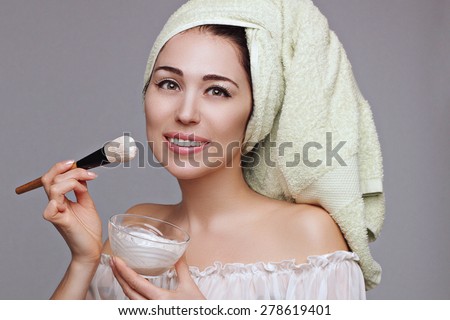 Young beautiful woman in towel turban applies cleansing mask using brush. White background. Skin care. Spa salon. Beauty and health.