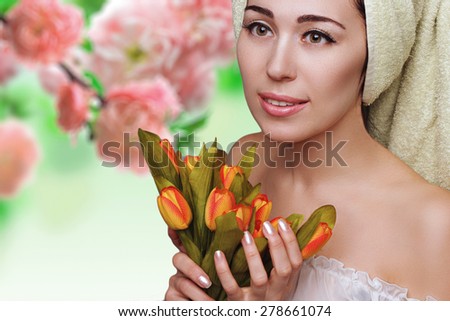 Young beautiful woman in towel turban with tulips flowers. Skin care. Spa salon. Beauty and health. Clear perfect skin.