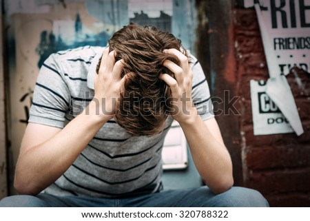 Emotionally depressed young male is sitting on the floor with his hands on the head