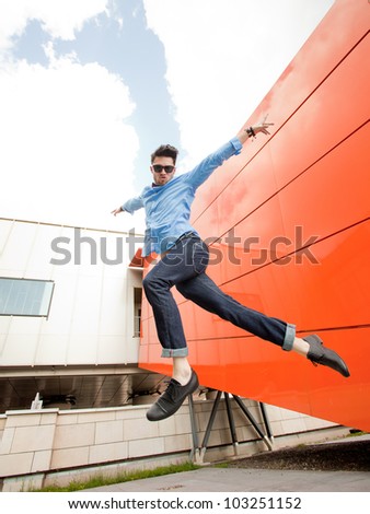 attractive young male model jumping outdoors in blue shirt and sunglasses