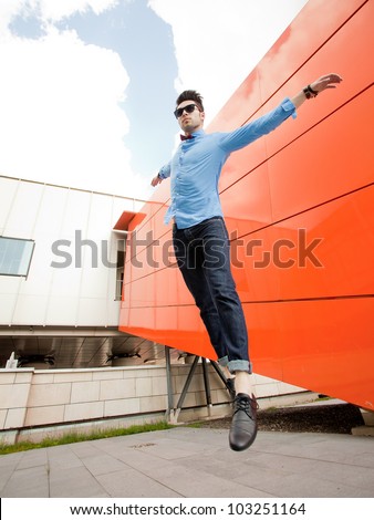 attractive young male model jumping outdoors in blue shirt and sunglasses