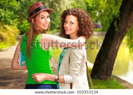 Two beautiful women walking and smiling in the park by the river - sunny day
