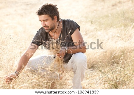 man on dry meadow picking grass straws to start a fire - into the wild series