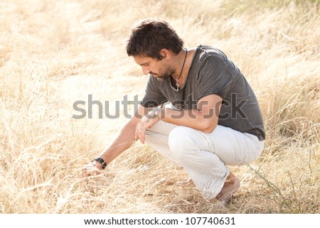 man on dry meadow picking grass straws to start a fire - into the wild series