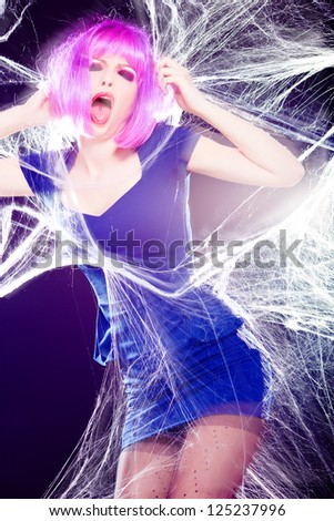 sexy woman with purple wig and intense make-up trapped in a spider web screaming- fashion shoot