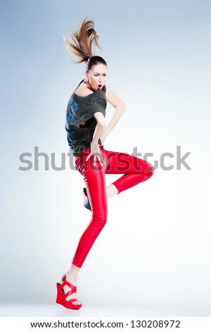sexy model with slim body dressed in red jumping and screaming in the studio against blueish background
