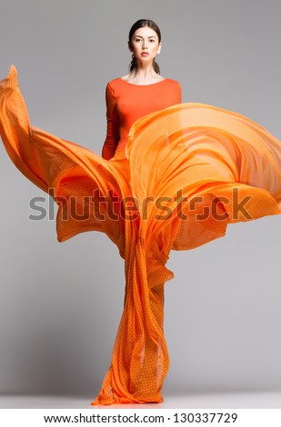 Beautiful Woman In Long Orange Dress Posing Dynamic In The Studio