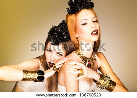two beautiful girls wearing make-up posing with gold accessories - studio shot