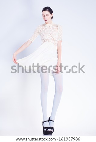 beautiful woman with long legs in white dress and high-heels posing in the studio
