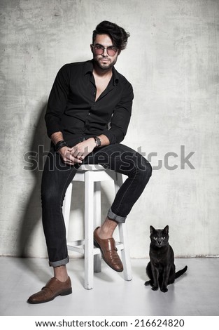 sexy fashion man model dressed casual posing with a cat against grunge wall